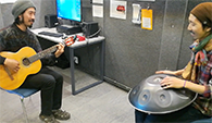 Two men playing guitar and handpan in the recording booth