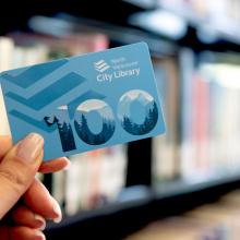 A photograph of a blue North Vancouver City Library card with blurred books in the background