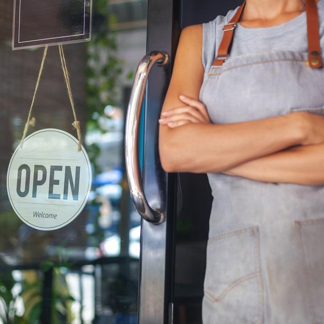 Woman in apron with crossed arms standing by door with open sign