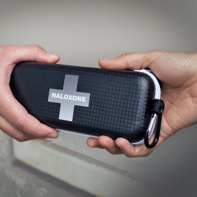 Two hands holding a rectangular kit with the naloxone logo in the middle