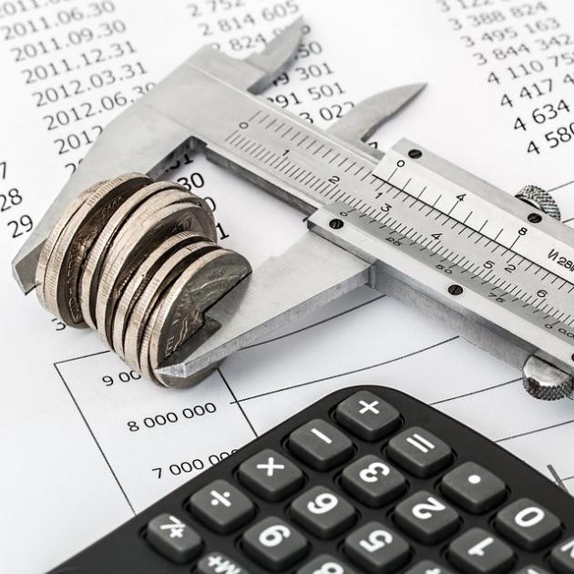 A calculator and a caliper squeezing a stack of coins together, sitting on a budget sheet