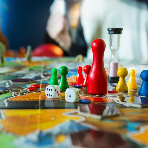 Board game with colourful pawns, timer and dice in foreground