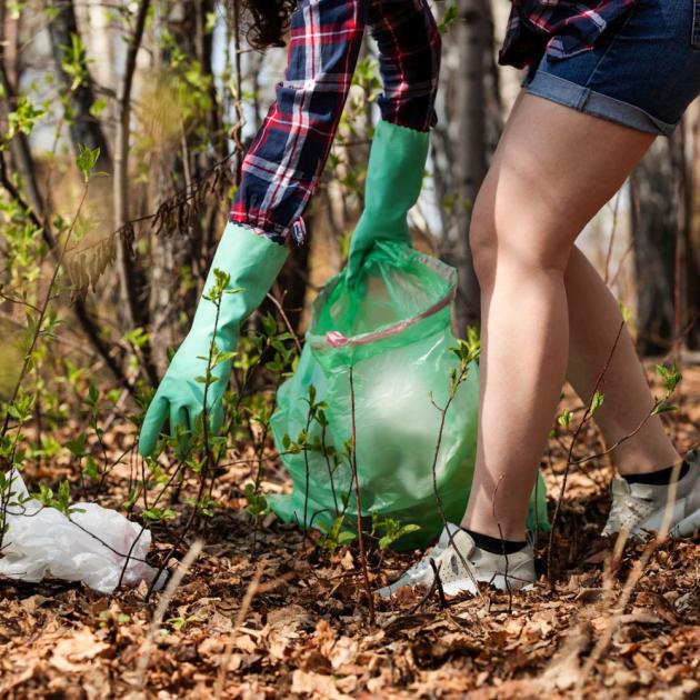 Person with gloves on, reaching down to collect garbage from the forest floor