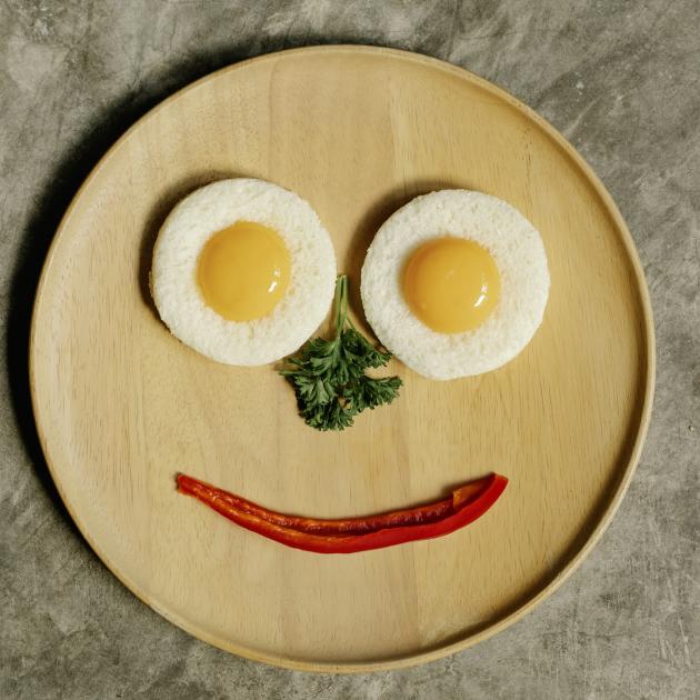 two eggs, a sprig of parsley and a piece of red pepper arranged on a plate in the form of a face