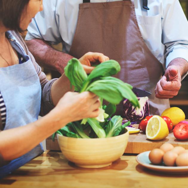 Two seniors preparing fresh spinach, vegetables, eggs, lemons