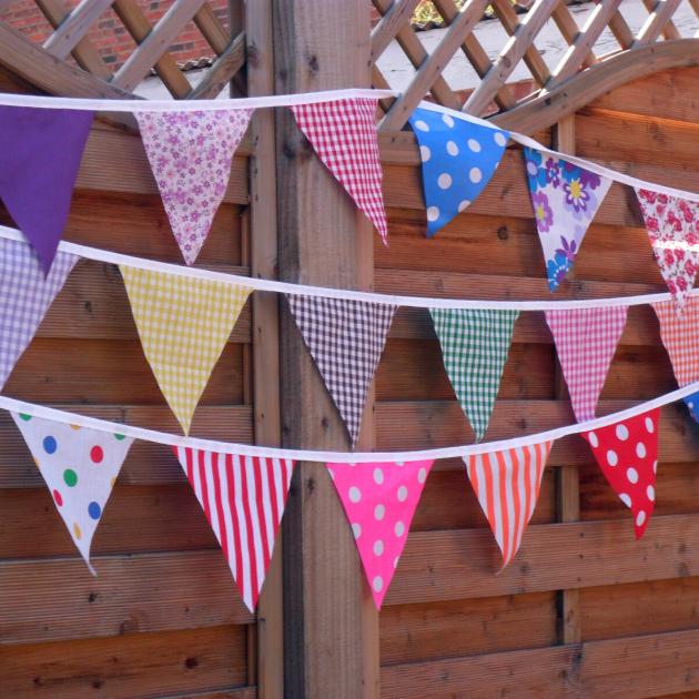 Three strings of bunting flags hanging in front of a wooden lattice fence.