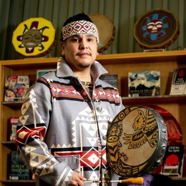 Dallas Guss holding a drum, with 3 drums on a shelf in the background