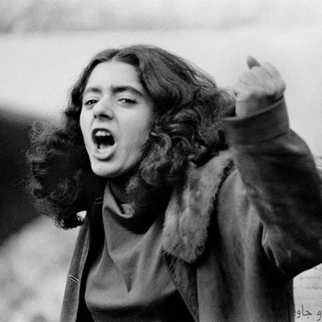 Young female with dark long hair chanting/yelling with her left fist up. 