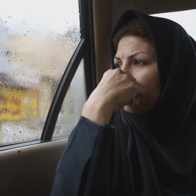 A female waring scarf sitting at the back of a car looking outside of the window. 