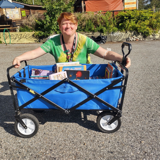 Staff member smiling as they crouch behind a small blue trailer full of books