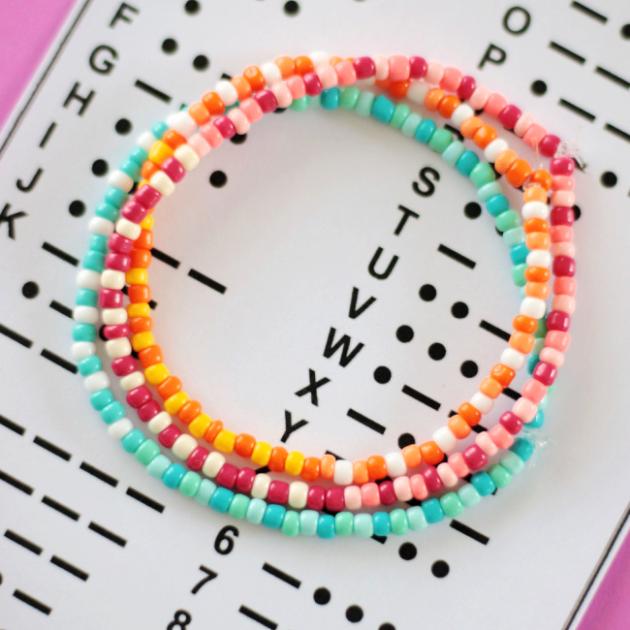 Three beaded bracelets sit on top of a Morse code chart.  