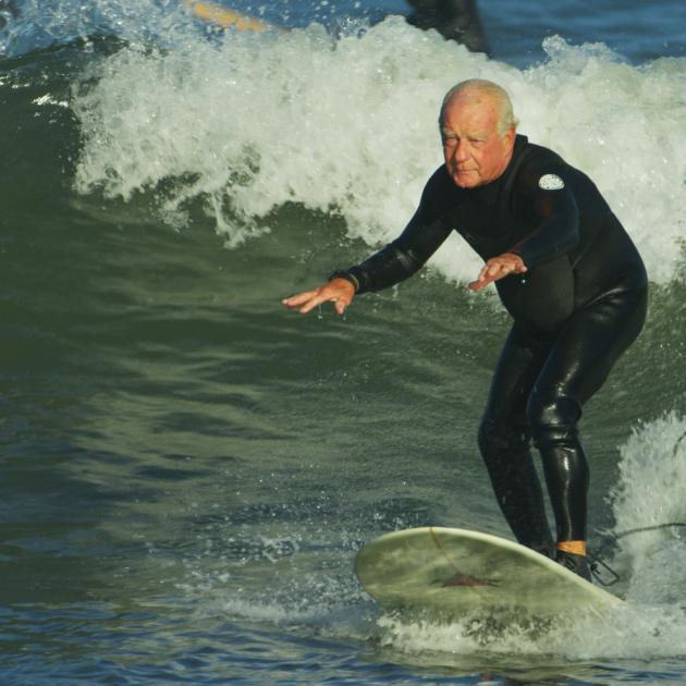 old white man with his arms stretched, wearing a bathing suit and surfing