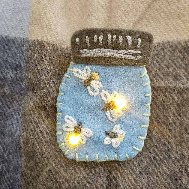 Button made of felt. Button is a jar with four fire-flies in it, two have LED's that light up. 