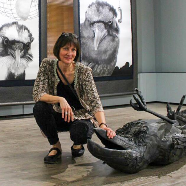 Woman crouches down next to crow sculpture in a gallery