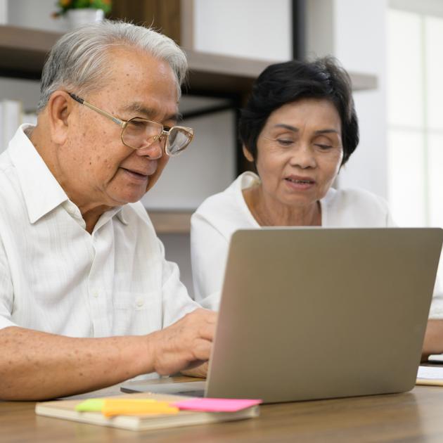 Two seniors sitting at a table, looking at a laptop screen