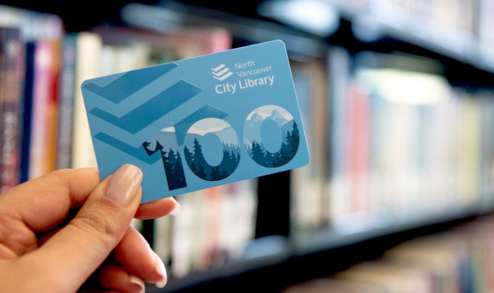 A photograph of a blue North Vancouver City Library card with blurred books in the background